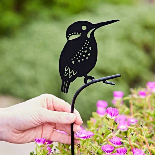 A hand places a Recycled Metal Kingfisher Silhouette Garden Stake among blooming pink flowers.