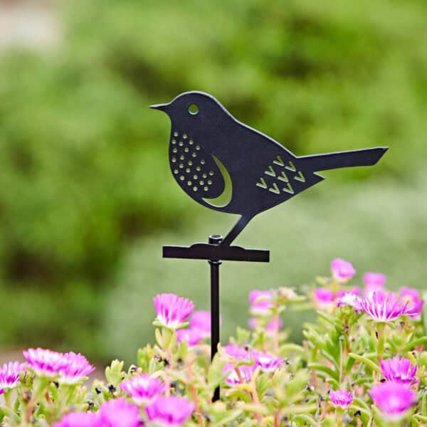 A Recycled Metal Robin Silhouette Garden Stake is placed among blooming pink flowers, standing out beautifully against the blurred green background.