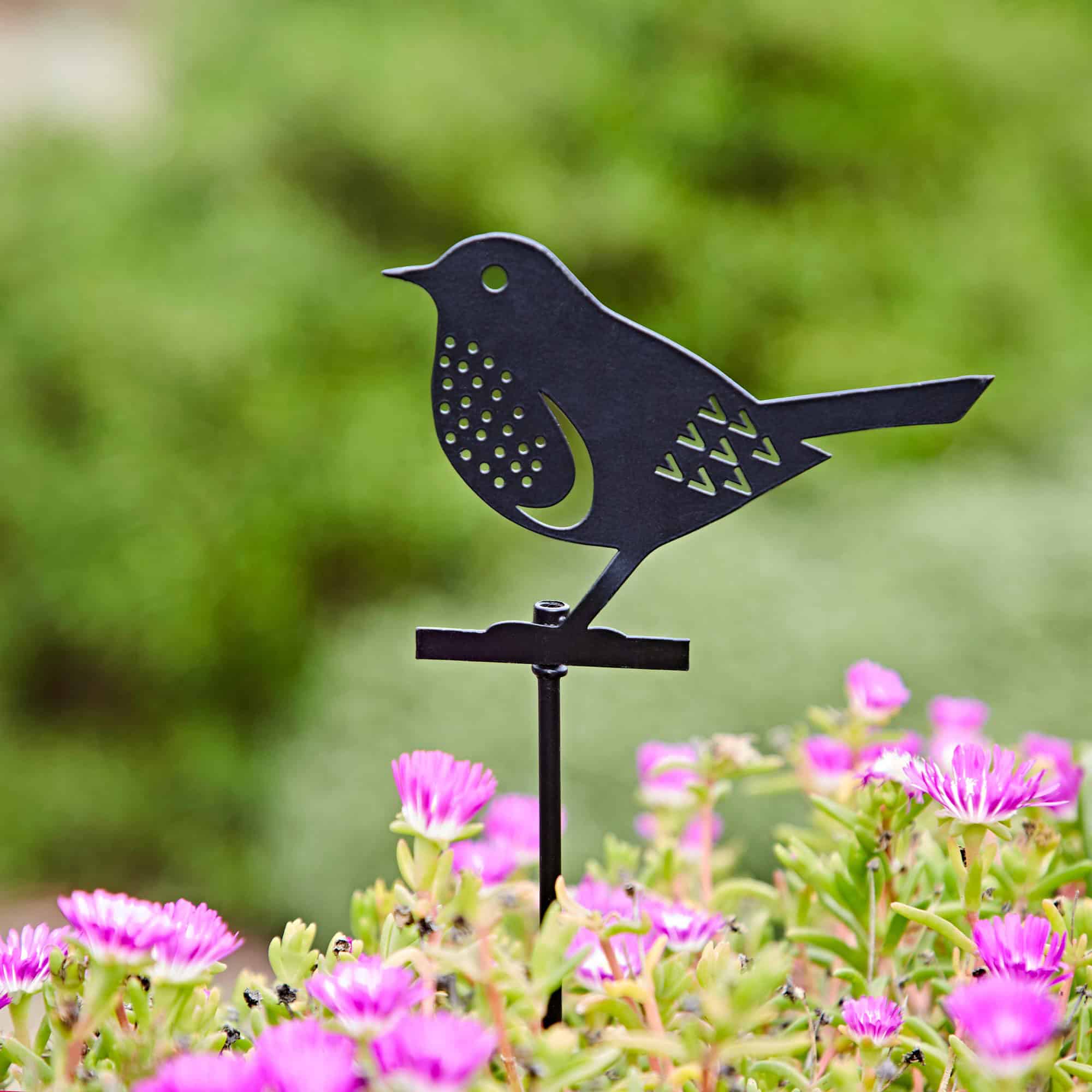 A Recycled Metal Robin Silhouette Garden Stake is placed among blooming pink flowers, standing out beautifully against the blurred green background.
