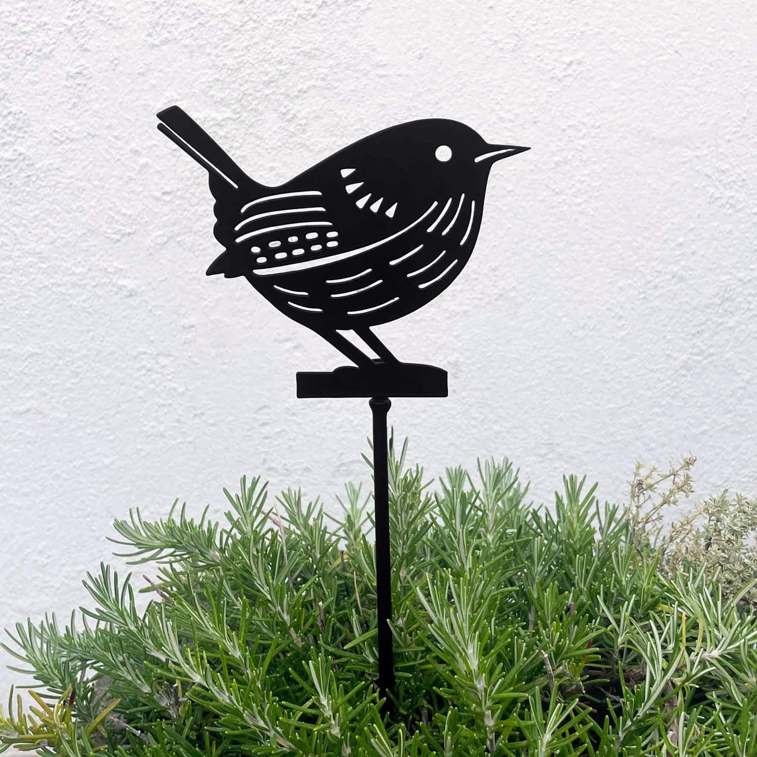 The Recycled Metal Robin Silhouette Garden Stake is shown among lush green foliage, set against a plain white wall.