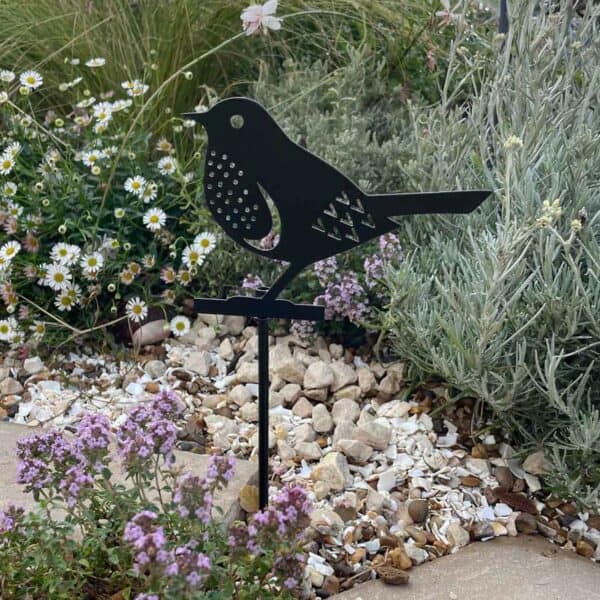 The Recycled Metal Wren Silhouette Garden Stake is crafted from recycled metal and adds charm among flowers, rocks, or greenery in any outdoor garden setting.