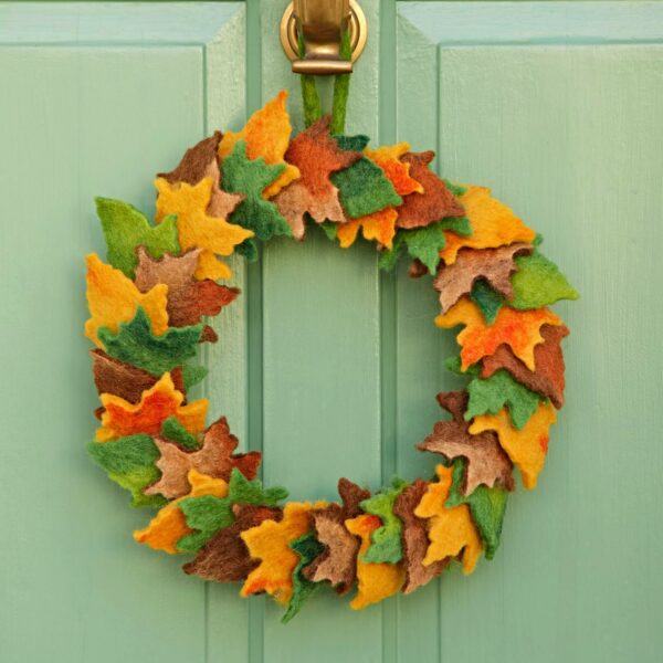 The Felt Woodland Autumn Wreath, crafted with green, yellow, brown, and orange felt leaves, hangs on a light green door to add cosy woodland charm to your entrance.