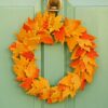 The Felt Autumn Leaves Wreath, featuring vibrant orange and yellow felt leaves, hangs beautifully on a green door.