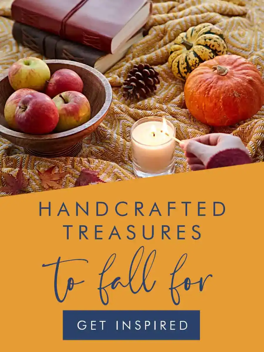 A hand lights a candle on a table with apples, pumpkins, pine cones, books, and a knitted blanket; text reads "Handcrafted treasures to fall for. Get inspired with Paper High finds.
