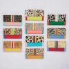 Twelve Hema Multicoloured Recycled Leather Clutch Purses with animal prints and colourful stripes are arranged in three rows on a light background.