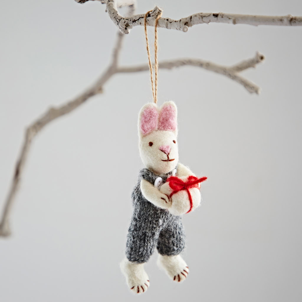 The Felt Rabbit with Gift Hanging Decoration features pink ears, a grey outfit, and holds a red and white present, making it a charming addition to any tree or branch.