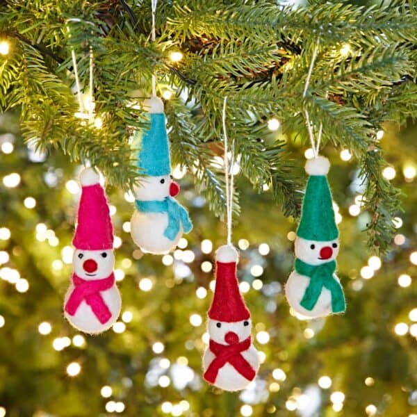 A Pack of 4 Colourful Felt Snowmen Christmas Decorations, each with bright hats and scarves, hangs from a Christmas tree branch as festive lights twinkle in the background.