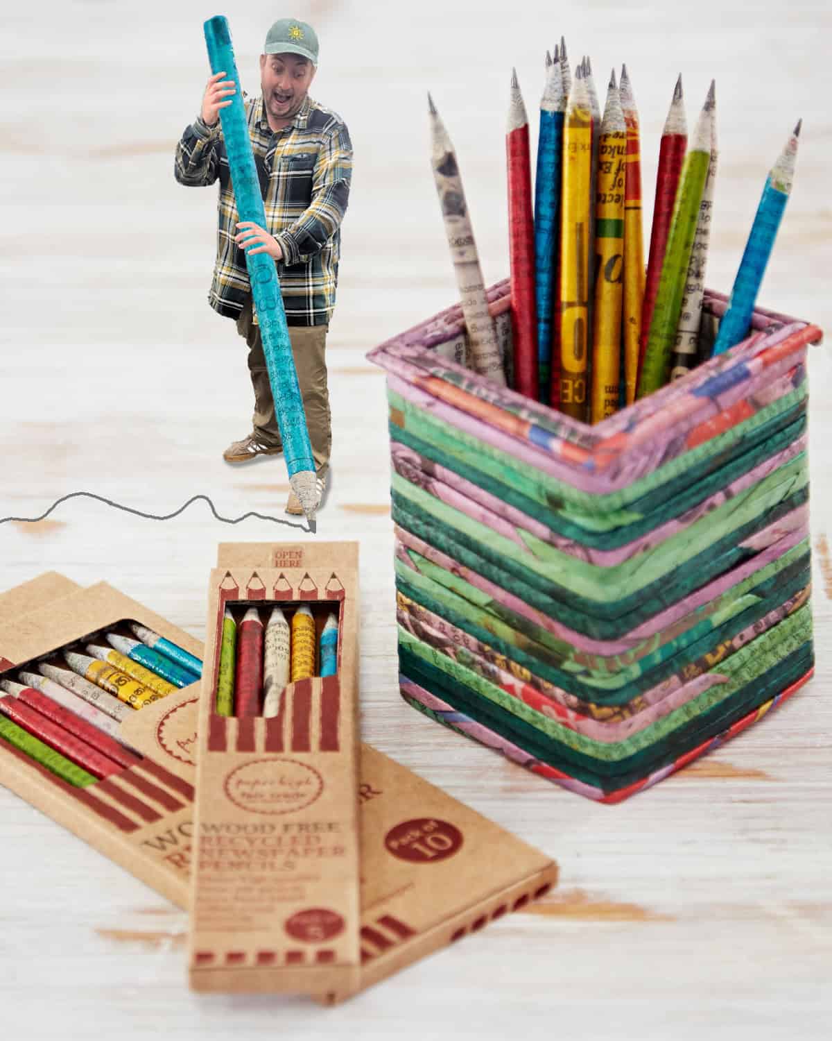 A person stands beside an oversized pencil, next to a pencil holder filled with colourful pencils and two boxes of wood-free pencils—perfect choices among our Staff Favourites for Christmas—on a light wooden surface.