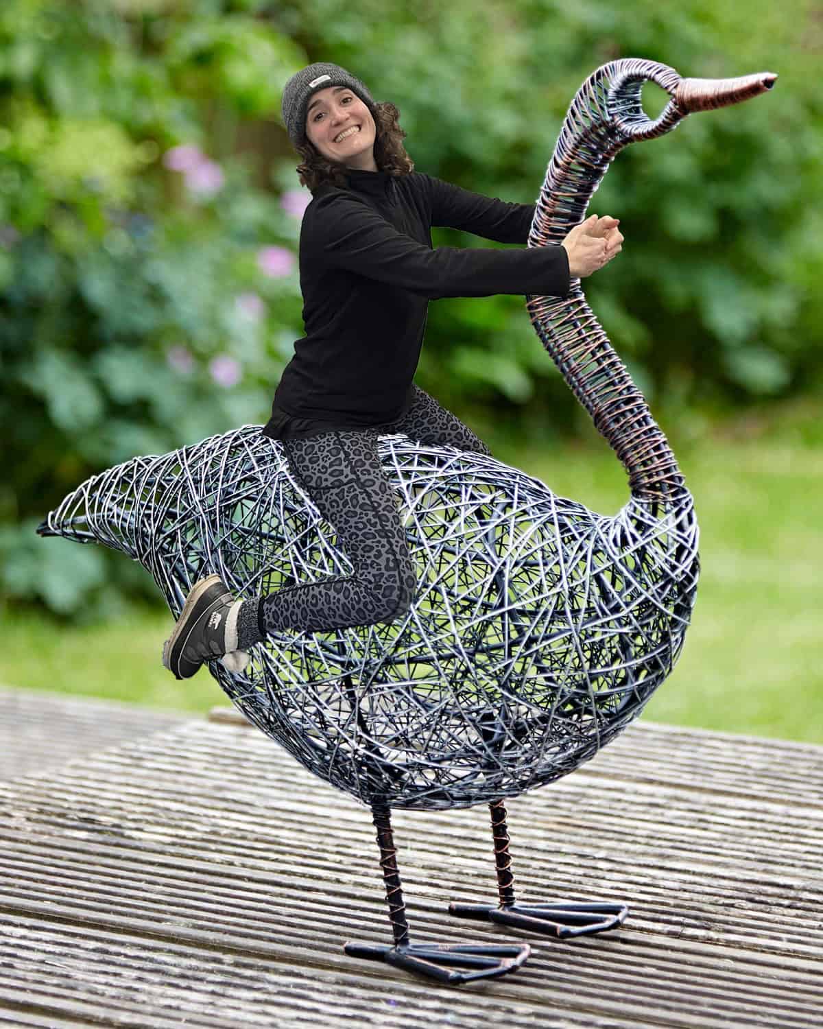 A person wearing a beanie and dark clothing sits on a large wire sculpture of a bird outdoors—a scene that could easily belong in our Staff Favourites for Christmas collection.