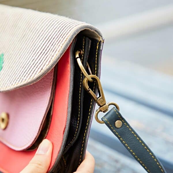 A close-up of a hand holding the Sonashki Multicoloured Rectangular Saddle Bag with a detachable strap, highlighting its metal clasp and detailed stitching.