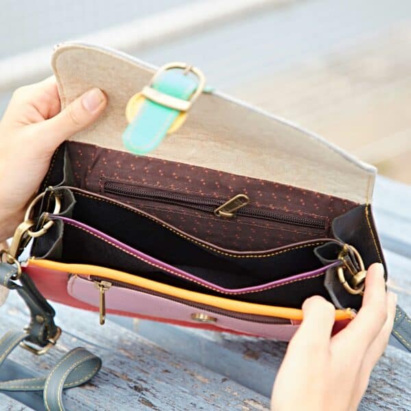 A person holds open the Sonashki Multicoloured Rectangular Saddle Bag, showing its empty interior with several compartments and a zipped pocket.