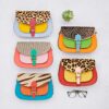 Six Sonashki Multicoloured Rectangular Saddle Bags with animal print flaps are arranged in two rows on a light surface, accompanied by a small succulent plant and spectacles.