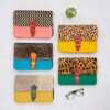 Six Multicoloured Recycled Leather Crossbody Buckle Bags with animal print and geometric patterns are displayed on a white surface next to a succulent plant and spectacles.