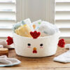 The Felt Chicken Storage Basket features a white fabric body with red felt accents and a cute chicken face, perfect for holding baby nappies and cloths. It sits near folded towels and a jar, keeping nursery essentials organised.