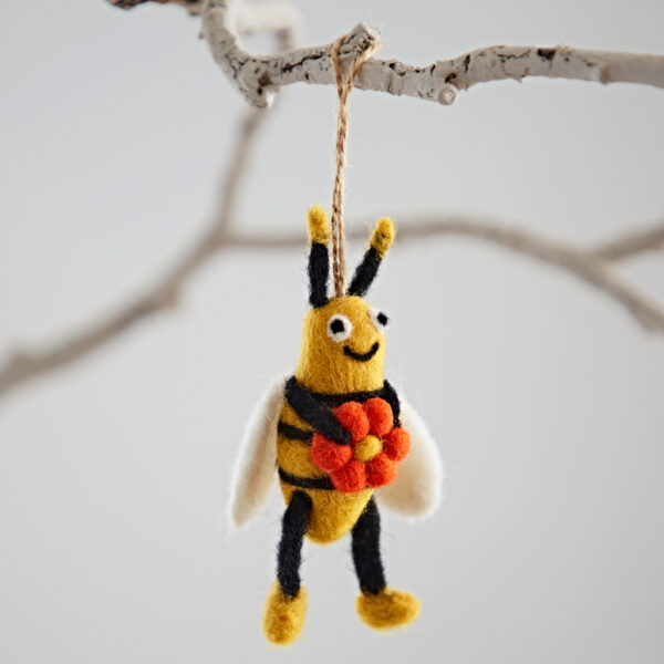 The Felt Bee with Flower Hanging Decoration features a bee holding red and orange flowers, charmingly hanging by a string from a white tree branch.