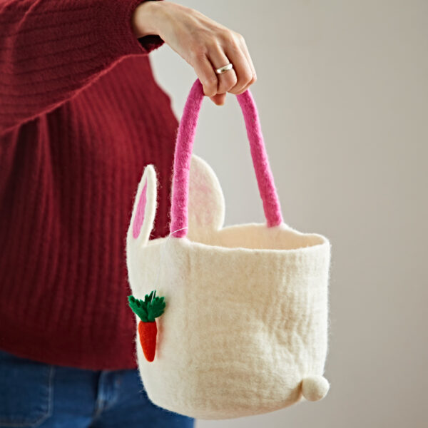 A person in a red jumper holds a Felt Easter Bunny Basket with Carrot Charm, featuring white felt, pink handles, bunny ears, a small pom-pom tail, and a carrot charm.