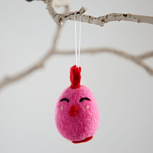 The Felt Easter Chick Hanging Decoration, shaped like a pink bird with a red crest, hangs from a white branch by a white string.