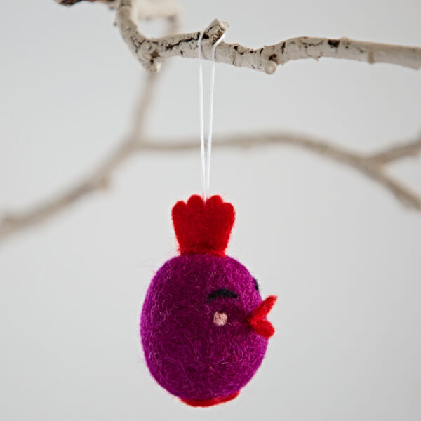 A Felt Easter Chick Hanging Decoration, shaped like a purple bird with a red crest and beak, hangs by a string from a white branch.