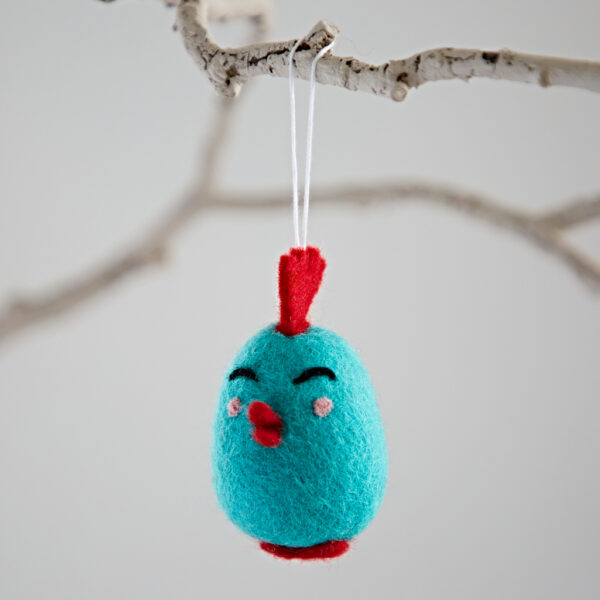 The Felt Easter Chick Hanging Decoration is a small, blue bird with red details that hangs from a string on a white branch.