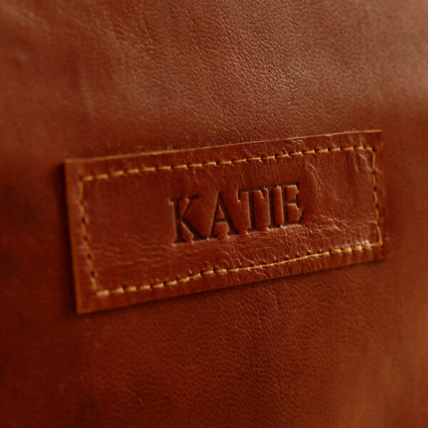 The Reworked Personalised Brown Leather Satchel features a brown leather patch embossed with the name 