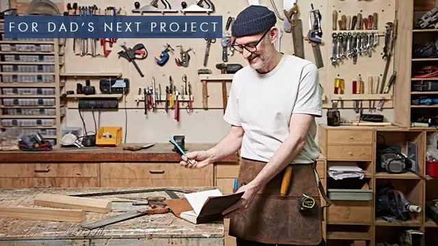 A man in a workshop stands at a workbench with tools, writing in a notebook on paper high with ideas. Text overlay reads, "For Dad's Next Project.