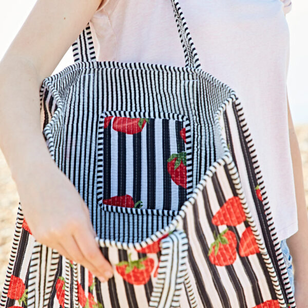 Person holding open a black-and-white striped bag with red strawberry prints, showing the empty interior and matching pocket.