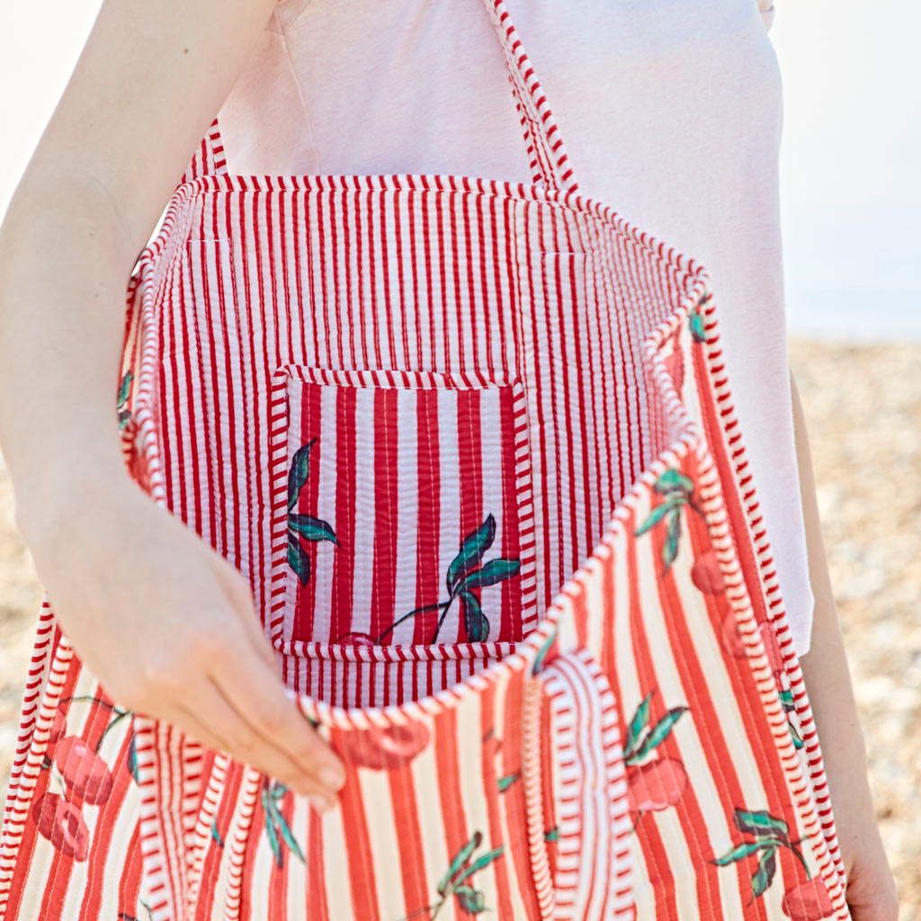 A person holds an open red and white striped bag with a cherry pattern, revealing the matching striped inner pocket.