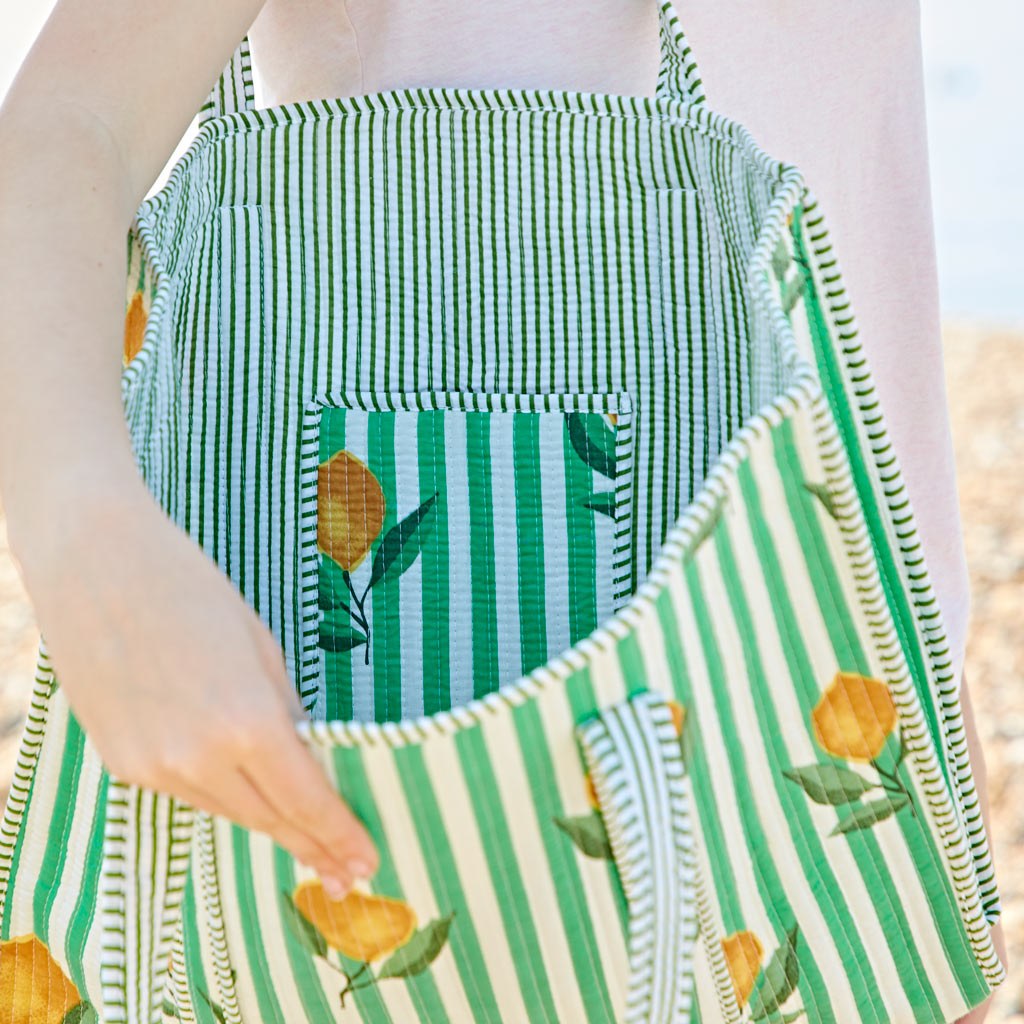 A person holds open a green and white striped bag with a lemon pattern, showing the interior and a small inner pocket.