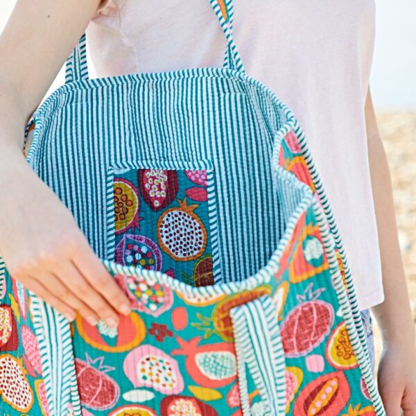 Person holding an open tote bag with a colourful pomegranate pattern and striped lining, showing the inside pocket.
