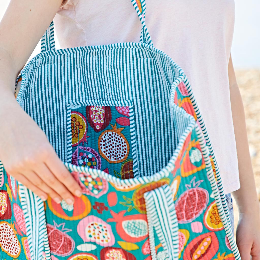 Person holding an open tote bag with a colourful pomegranate pattern and striped lining, showing the inside pocket.
