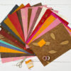 Sheets of colourful decorative paper from the Handmade Lokta Paper Craft Pack are fanned out on a white background, accompanied by scissors, twine, and rolls of washi tape placed alongside.