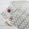 Several sheets of grey and white patterned paper, a pair of gold scissors, two rolls of decorative tape, and a labelled envelope from the Handmade Silver Heart Craft Pack are displayed on a white wooden surface.
